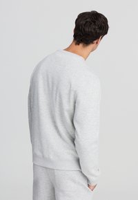 Felpa grigia chiara con scollo rotondo e maniche lunghe. Realizzata in materiale morbido, presenta una vestibilità comoda e polsini a coste.