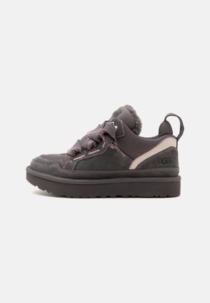 Mørkegrå UGG sneaker med tyk sål, pink syninger, polstret krave, mesh sektioner og brede snørebånd mod en ensfarvet lys baggrund.
