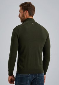 Dunkelgrüner gestrickter Pullover mit einem Reißverschlusskragen, gerippten Bündchen und einer aufgesetzten Tasche am linken Arm. Glatte Textur und taillierter Schnitt.