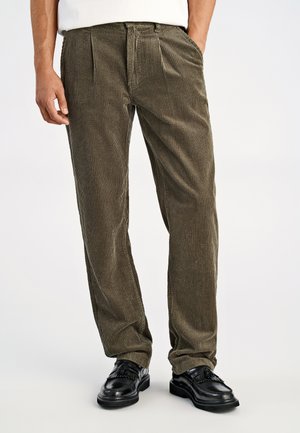 Pantaloni in velluto a coste verde oliva con una texture liscia, dotati di tasche laterali e vestibilità comoda, abbinati a scarpe eleganti nere.