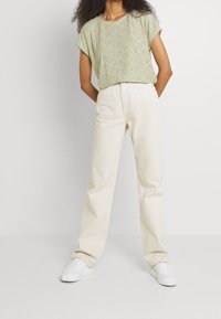 Haut vert clair à manches courtes avec un design perforé, associé à un pantalon beige taille haute et jambes droites, ainsi qu'à des baskets blanches.