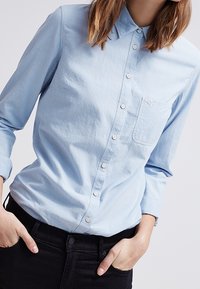 Ljust blå, långärmad skjorta med krage och bröstficka. Har en avslappnad passform och mjuk bomullstyg.