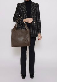 Sac en cuir brun avec une finition texturée, forme carrée et une étiquette accrochée. Assorti à un blazer à carreaux noir et blanc.