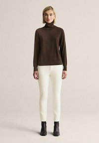 Brun polotröja med långa ärmar, ihopparad med vita slim fit-byxor och ankelstövlar. Texturerad tyg och åtsittande design.