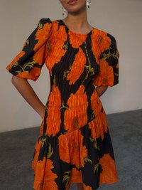 Abito nero con un vivace motivo floreale arancione, caratterizzato da maniche a sbuffo, un corpetto plissettato e una gonna svasata. Tessuto di superficie liscia.