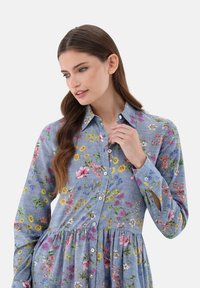 Abito camicia floreale in stoffa blu, caratterizzato da fiori colorati assortiti, apertura con bottoni, colletto e gonna a pieghe con maniche lunghe.