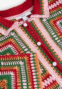 Cárdigan de ganchillo multicolor con patrones en rojo, verde, naranja y rosa. Diseño completado con botones delanteros y un cuello redondeado.