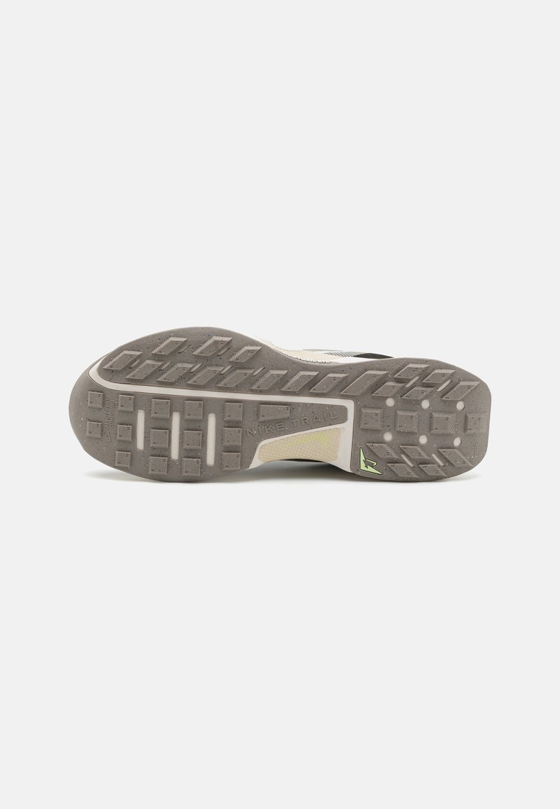 Semelle de chaussure de trail running avec un design en caoutchouc beige et gris, dotée de motifs de grip texturés, d'un logo proéminent et d'une accentuation verte.