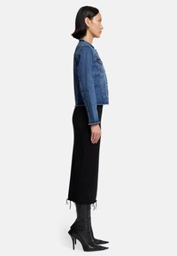 Blaue Jeansjacke mit einem verkürzten Design, ausgefransten Kanten und zwei Fronttaschen. Kombiniert mit einem schwarzen langen Rock und schwarzen spitzen Absatzstiefeln.