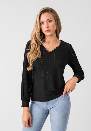 Black long-sleeve top with scalloped neckline, textured lace pattern, and balloon sleeves. Paired with light blue jeans.