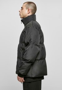 Jachetă puffer neagră cu guler înalt, design matlasat, buzunare laterale și manșete elastice. Textură netedă, croială de lungime medie.