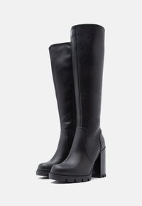 Botas de cuero negro hasta la rodilla, con tacón cuadrado, cremallera lateral y suela gruesa con detalles acanalados.