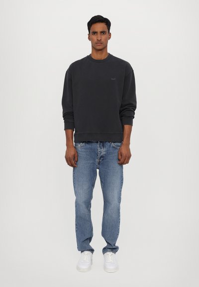 Sweatshirt à col rond gris foncé avec des poignets côtelés, associé à un jean en denim bleu clair et des baskets blanches. Design simple et décontracté.