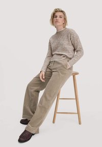 Beige gebreide trui met een textuurpatroon, gecombineerd met hoogstaande, tan corduroy broeken; model draagt donkeren bruine loafers.