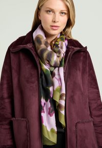 Abrigo burdeos con textura y diseño con cremallera, superpuesto sobre una camiseta negra, complementado con una bufanda colorida de estampado floral en tonos verdes y rosas.