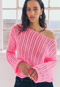 Maglione rosa lavorato a maglia con design off-shoulder, vestibilità ampia con maniche larghe e un motivo a trama aperta.