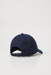 Navy blue cap made of cotton with a curved brim, adjustable strap at the back, and textured surface with panel stitching details.