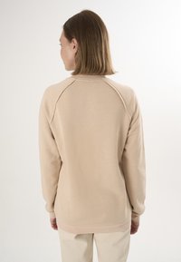 Felpa beige con maniche raglan, texture liscia e polsini a coste. Collo rotondo e orlo del retro leggermente più lungo.