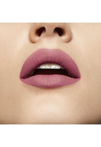 Rouge à lèvres mat dans une couleur mauve doux sur des lèvres lisses, mettant en valeur une forme bien définie avec une texture subtile et un éclat naturel sur les dents.