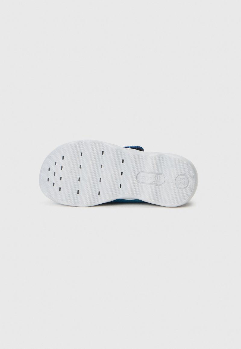 Weiße Gummisohle mit strukturiertem Grip, runder Form und oberem Material aus blauer Textilie. Enthält Belüftungsöffnungen und Markierungsdetails an der Seite.