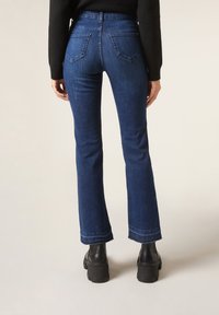 Jean flare en denim, avec une taille haute, deux poches arrière et un ourlet brut aux chevilles, associé à des bottes à plateforme noires.
