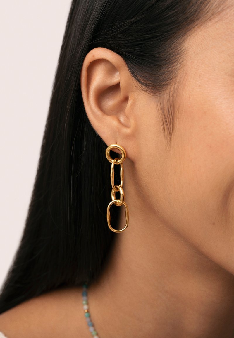 Pendientes de metal dorado con un diseño de cadena enlazada que presenta formas ovaladas y redondas de diferentes tamaños. Textura suave con un acabado pulido.