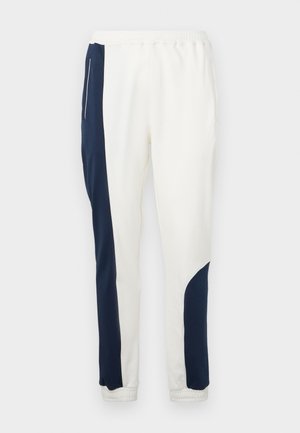 Biele teplákové nohavice so námornícky modrými bočnými panelmi a elastickými manžetami, vyrobené z mäkkého materiálu s hladkou textúrou a sťahovacím pásom.