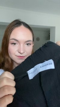 Svart tygblus med en texturerad yta, med en vit etikett som visar varumärket "Bershka". Synlig sömnad och inga framträdande detaljer.