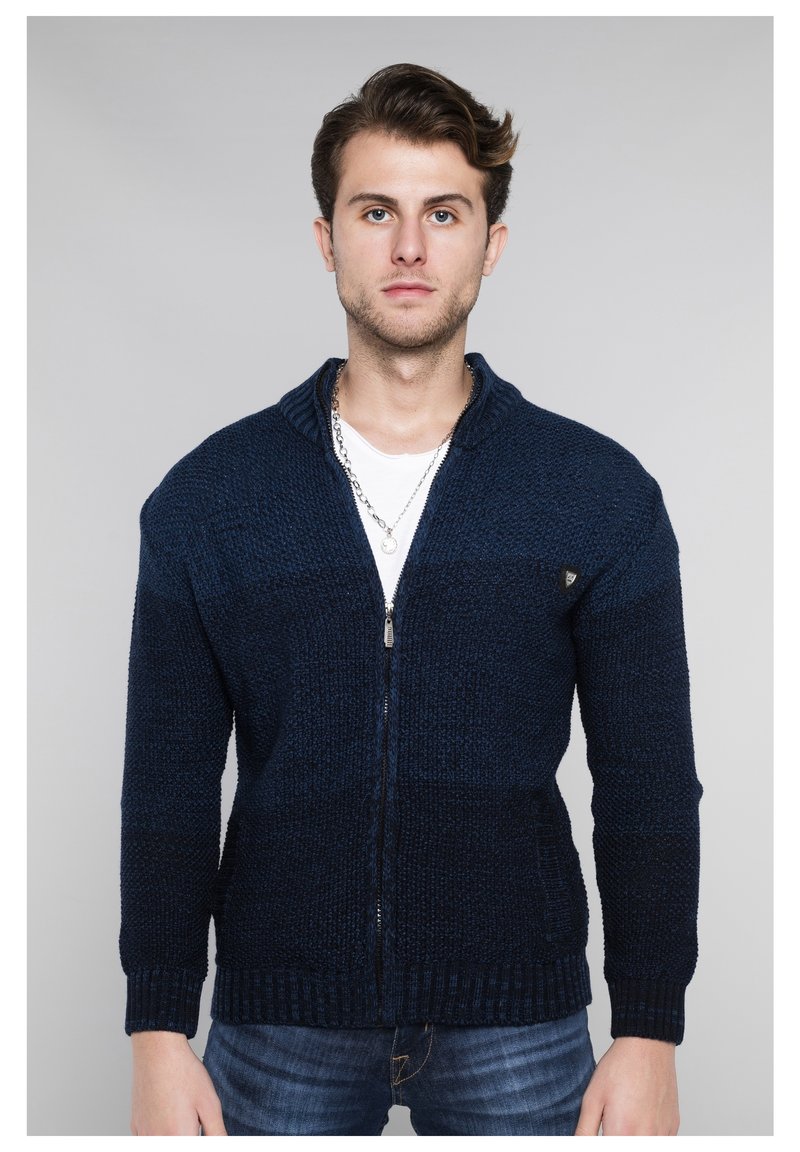 Marineblauer gestrickter Reißverschluss-Kardigan mit strukturiertem Muster, hohem Kragen und gerippten Bündchen. Verfügt über seitliche Taschen und dezente Logodetails.