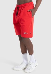 Rode shorts van een katoenmix met een elastische tailleband, voorzien van zijzakken en een wit logo op de linker dij.