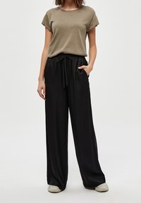 Olivgrön texturerad t-shirt med korta uppvikta ärmar, i kombination med högmidjade svarta vida byxor som har elastisk dragsko i midjan.