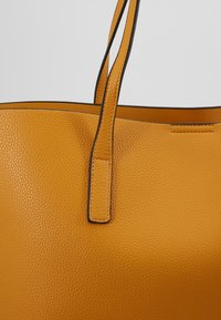 Borsa a tracolla in pelle texturizzata giallo senape con due manici sottili e dettagli neri sui bordi.