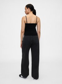 Top cropped preto ajustado com alças finas, combinado com jeans pretos de perna larga. Ténis com detalhes brancos e design de perfil baixo. Visual minimalista.