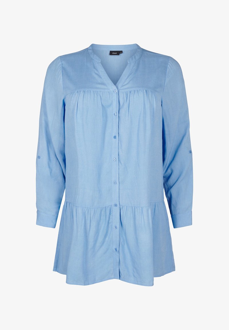 Gaiši zils krekls ar pogām, izgatavots no mīksta auduma. Iezīmēts ar apkakli, savākto krūšu daļu un garām piedurknēm ar pogām.