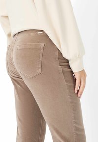 Bruine ribfluwelen broek met een aansluitend ontwerp, voorzien van twee achterzakken en een zachte textuur. De tailleband zit op de natuurlijke taille.