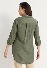 Olijfgroene, gestructureerde longsleeve shirt met een rugplooi, knoopmanchetten en een afgeronde zoom. Gemaakt van een lichtgewicht, geribbeld materiaal.