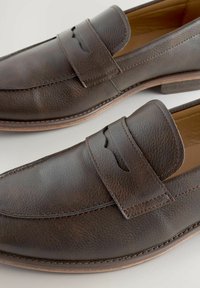 Mocasines de cuero marrón con un acabado texturizado, que presentan un vampiro cosido y un sutil detalle de corte. Tacón bajo apilado y un interior suave.