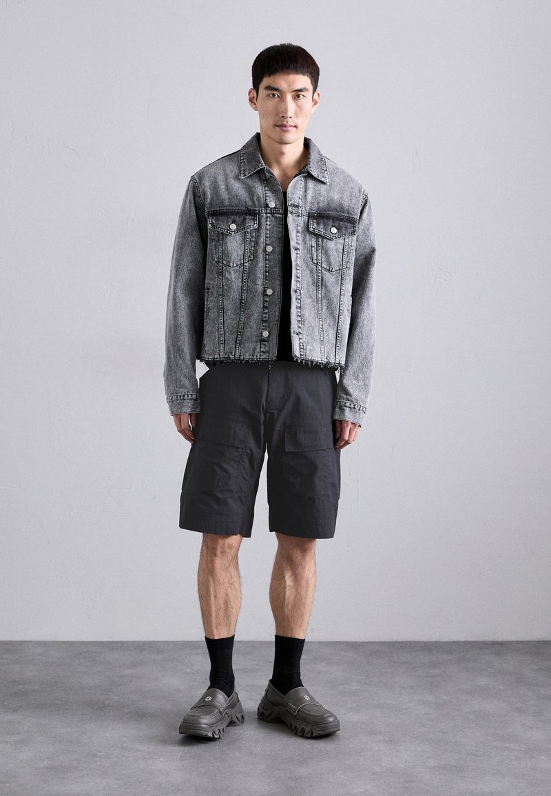 Veste en jean grise avec deux poches poitrine, associée à un short cargo noir et des chaussures grises à enfiler. Design simple, coupe décontractée.