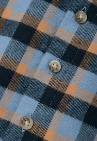 Camicia di flanella con un motivo a quadri blu, nero e arancione, con bottoni beige ben visibili e un tessuto morbido e strutturato.