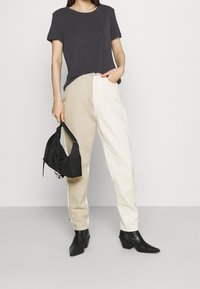 Svart kortärmad t-shirt kombinerad med byxor som är halva beige och halva vita, med smal passform. Svart väska med remmar. Fyrkantig stövlar med klack. Släta texturer.