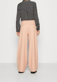 Světlé růžové kalhoty širokého střihu s přiléhavým pasem a zadními kapsami, doplněné černobílým pruhovaným topem s dlouhými rukávy.
