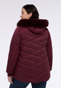 Burgundowa puchowa kurtka z odpinanym kapturem z sztucznego futra, z ukośnym pikowaniem i luźnym krojem. Miękka, błyszcząca tkanina zewnętrzna.