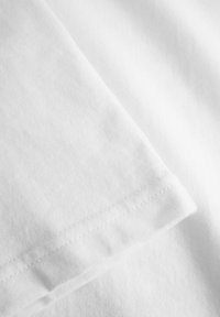 Țesătură albă din bumbac cu o textură fină, având o margine pliată și detalii de cusătură subtile, evidențiind designul său simplu.