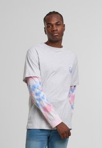 Grå bomulls t-skjorte med et fargerikt tegneseriedesign på brystet, kombinert med lange batikk-sleeves i rosa, blått og hvitt.