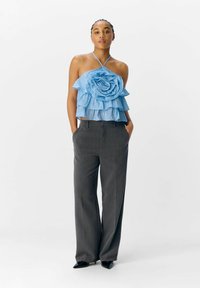 Top halter azzurro chiaro a strati con un grande accentuato a rosa, abbinato a pantaloni grigi a vita alta con gamba larga e tacchi neri a punta.
