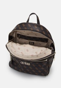 Mustavälinen nahkareppu, jossa on kultainen logo ja kohokuvioitu malli. Reppu on varustettu vaaleanbeigellä sisätilalla ja vetoketjullisilla lokeroilla järjestystä varten.