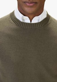 Olivgrön stickad tröja med rund hals, ribbat nederkant och texturerad tyg, lager-på-lager över en vit skjorta med krage.