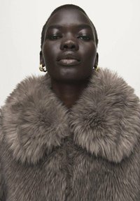 Graue Kunstpelzjacke mit großem, flauschigem Kragen. Verfügt über eine weiche Textur und eine abgerundete Form, die Wärme und Komfort erhöht.