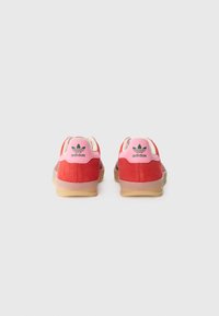 Rode suède sneakers met roze accenten, voorzien van een gumrubberen zool en het Adidas-logo op de hiel. Ontworpen voor casual gebruik.