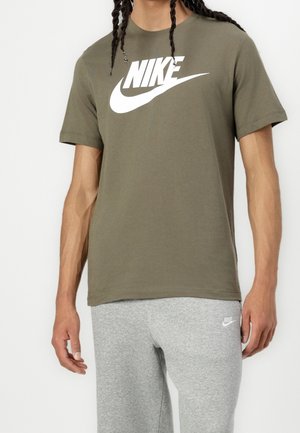 Zielono-oliwkowa bawełniana koszulka z okrągłym dekoltem, z widocznym białym logo Nike. W połączeniu z szarymi dresami.